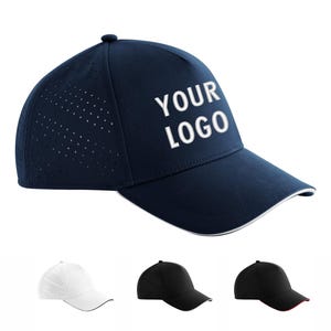 May include: A navy blue baseball cap with white text reading YOUR LOGO on the front panel. The side panels feature a perforated design for ventilation, and the curved brim has a thin white trim along the edge. Three additional caps are shown below.