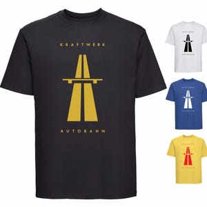May include: Black t-shirt with the word "KRAFTWERK" above a yellow highway overpass graphic, and "AUTOBAHN" below. Other shirts in white, blue, and yellow with the same design are also displayed.