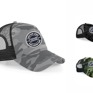 May include: Three trucker hats featuring a camouflage pattern in gray, black, and green. Each hat has a black mesh back and a circular patch on the front with the text CUSTOM LOGO YOUR DESIGN HERE. The hats have a curved brim and a structured front panel.