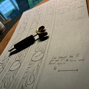 May include: A close-up of a leather carving pattern with a pencil drawing of a floral design. The text "Line Should be 1"  If not 1" de Scule and Print aguin" is written on the paper. A ruler is drawn with a measurement of 15.24 cm.
