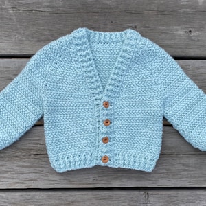 Può includere: Un cardigan in crochet blu chiaro con scollo a V e chiusura con bottoni. Il cardigan ha un motivo a punto testurizzato ed è realizzato con un filato morbido.