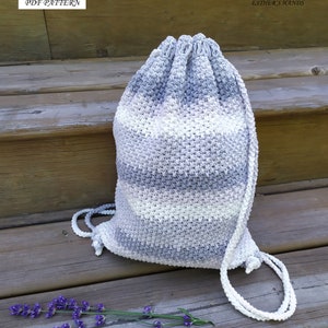 May include: A crocheted drawstring bag with a white and gray striped pattern. The bag is sitting on a wooden surface with a sprig of lavender in the foreground. The text "PDF PATTERN" and "ESTHER'S HANDS" is visible in the image.