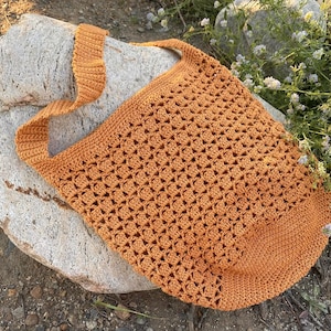 May include: A crocheted tote bag with a brown strap. The bag is made of a lightweight, open weave material and has a relaxed, casual style.
