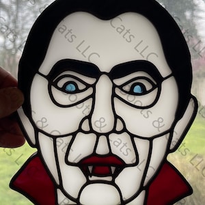 May include: A stained glass window hanging features a black and white illustration of a vampire with blue eyes, a red collar, and a yellow bow tie.