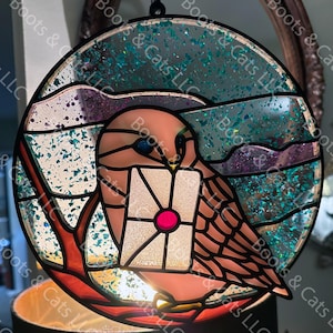 May include: A stained glass owl holding a white envelope with a pink heart in the center. The owl is perched on a branch with a blue and green background.