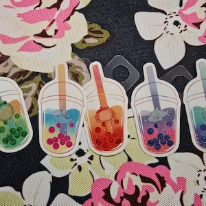 May include: Five die-cut stickers featuring bubble tea cups with gradient colors. Each cup contains a different animal: a green frog, a blue seal, an orange axolotl, a grey shark, and a teal narwhal, all with matching colored boba pearls.