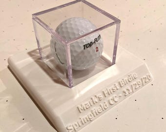 May include: A white golf ball with the text "TOP-FLITE" and the number "2" is displayed in a clear plastic cube on a white base. The base is inscribed with the text "Mark's First Birdie Springfield CC - 11/29/20"