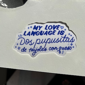 K&ouml;nnte beinhalten: Ein wei&szlig;er Aufkleber mit blauem Text, der "My love language is Dos pupusitas de frijoles con queso." lautet.