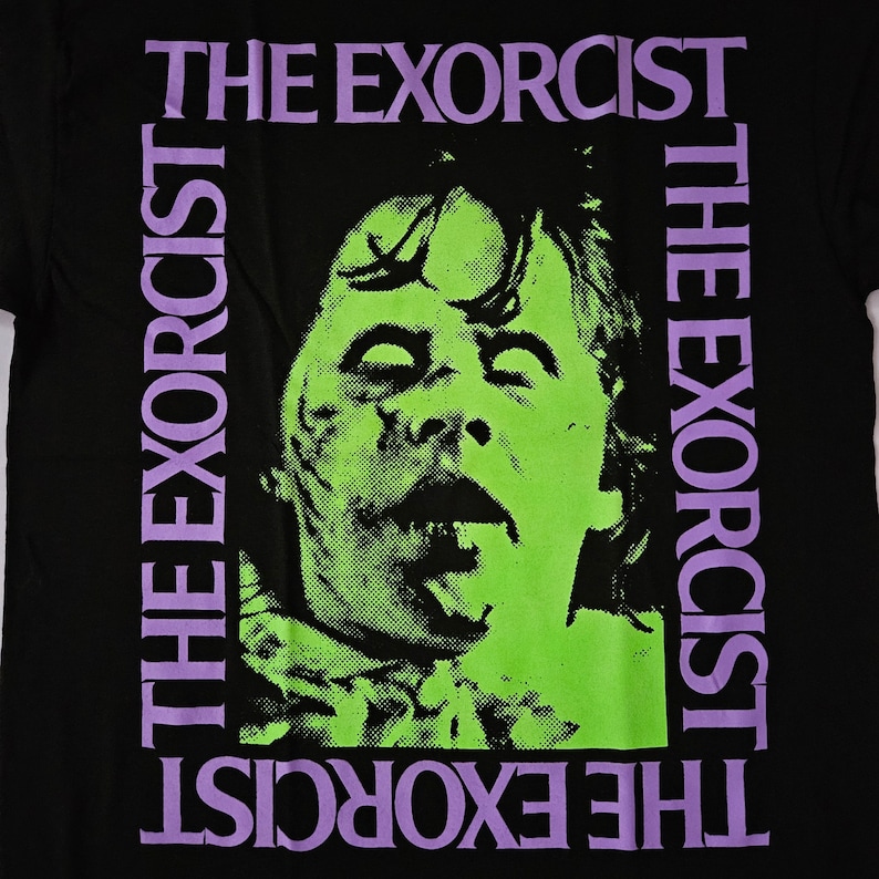 May include: Black t-shirt featuring a green and purple graphic of a face with its mouth open and tongue sticking out. The text "THE EXORCIST" is printed in purple on the left and right sides of the graphic.