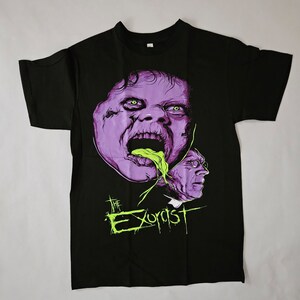 May include: Black t-shirt featuring a purple and green graphic of a demon from the film "The Exorcist".