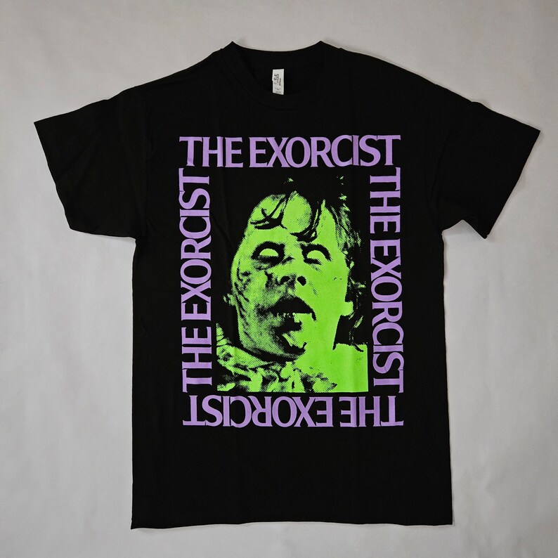 May include: Black t-shirt featuring a green and purple graphic of a face from the film "The Exorcist". The text "The Exorcist" is repeated four times on the shirt.