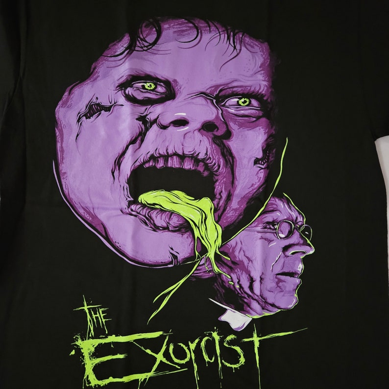 May include: Black t-shirt featuring a green and purple illustration of a demon from the film "The Exorcist".