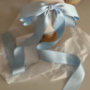 May include: A light blue satin ribbon tied into a large bow. The ribbon is long and flowing, with the ends trailing down.