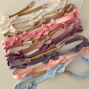 Puede incluir: Un conjunto de 12 cintas para el pelo con lazos de satén en varios colores pastel, incluyendo rosa, morado, azul y beige. Las cintas para el pelo están hechas con elástico y tienen una banda de color carne.