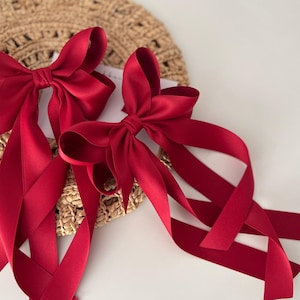 May include: Two large red satin bows with long tails. The bows are tied together and are on a white background.
