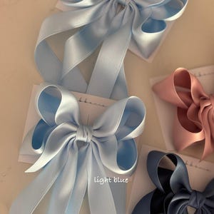 May include: Three satin ribbon hair bows in different colors: light blue, pink, and navy blue. The light blue bow has the text "light blue" written below it.
