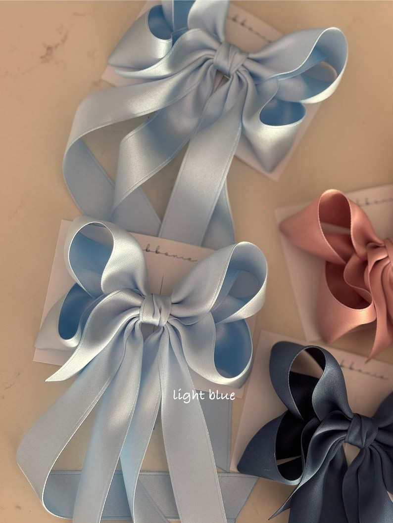 May include: Three satin ribbon hair bows in different colors: light blue, pink, and navy blue. The light blue bow has the text "light blue" written below it.