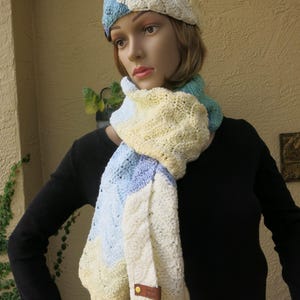 May include: A crocheted headband and scarf set in shades of blue, yellow, and white. The headband is a wide band with a simple stitch pattern. The scarf is a long, rectangular shape with a more intricate stitch pattern. The set is made with a soft, lightweight yarn.