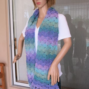 Puede incluir: Una bufanda de ganchillo con un patrón multicolor de morado, azul y verde. La bufanda tiene flecos en la parte inferior.