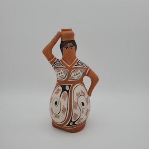 May include: A terracotta figurine of a woman carrying a vessel on her head. The figure is painted with brown, black, and white geometric patterns. The woman's skin is a light brown color, and she has black hair.