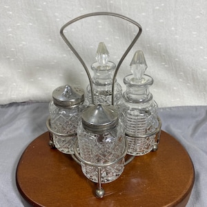 May include: A vintage glass condiment set with a silver metal stand. The set includes two small bottles with crystal stoppers, two shakers with perforated lids, and a handle. The glass bottles have a diamond pattern.