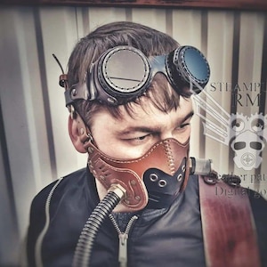 May include: A person wearing a brown leather steampunk gas mask with a black and brown strap. The mask has a metal nose piece and a metal tube coming out of the side. The person is also wearing goggles with round lenses.