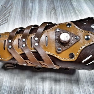 Pode incluir: Pulseira steampunk de couro marrom com um painel de couro bege e detalhes em metal. A pulseira tem um design decorativo com tiras e rebites. A pulseira é um padrão de download digital.