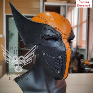 May include: A black and orange leather mask with a steampunk design. The mask has a pointed top and a large eye opening. The mask is on a mannequin head.