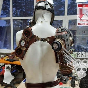 May include: A steampunk-style leather and metal chest harness with a gas mask and gauges. The harness is brown and has a metal buckle. The gas mask is black and has a metal mouthpiece. The gauges are silver and have black numbers. The harness is worn on a white mannequin.