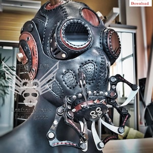 May include: A black leather steampunk gas mask with red and brown leather trim. The mask has a large round eye piece and a smaller round nose piece. The mask is attached to a metal frame with a series of gears and levers. The mask is on a wooden table.