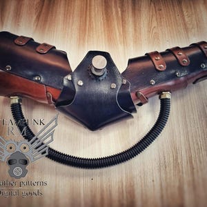 Op de afbeelding: Een steampunk-achtige leren armbrace met een zwarte leren elleboogbeschermer en een zwarte rubberen slang eraan bevestigd. De brace heeft bruine leren banden en metalen klinknagels. De tekst "STEAMPUNK RM" is zichtbaar op de afbeelding.