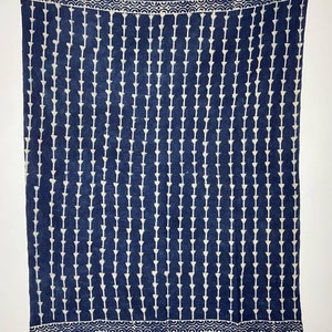 Op de afbeelding: Een blauwe katoenen deken met een wit geometrisch patroon. De deken heeft een franje rand.