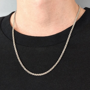 Puede incluir: Un collar de cadena de plata en una persona que lleva una camisa negra.