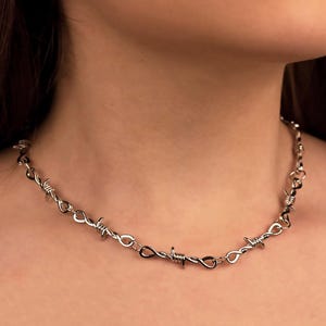 May include: A silver necklace with a barbed wire design. The necklace is made of metal and has a twisted, barbed wire look.