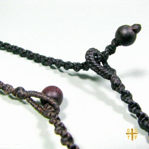 Puede incluir: Primer plano de un collar de cordón negro con cuentas de madera marrón oscuro. El cordón está anudado y atado para formar un bucle.