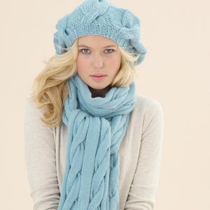 May include: A light blue knitted beret and scarf set. The beret has a cable knit design, and the scarf is long and also features a cable knit pattern. The set is made of a soft, warm material, perfect for cold weather.