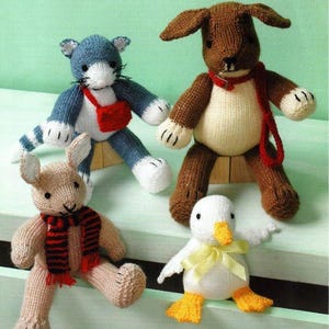 May include: Four knitted animal toys: a blue cat with a red bag, a brown dog with a red collar and leash, a tan bunny with a red and black scarf, and a white duck with a yellow bow.