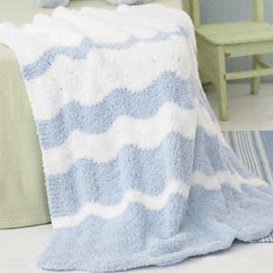 Pode incluir: Um cobertor macio e felpudo em tons de branco e azul claro. O cobertor apresenta um padrão ondulado, com listras alternadas brancas e azul claro. O cobertor está sobre uma cama.