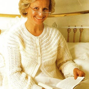 May include: Cream-colored, open-front cardigan with a textured knit pattern. The cardigan has a round neckline and button closures. The image also shows a book and the text "81-117 cm 32-46 in".