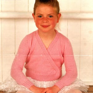 May include: A pink wrap-style cardigan with long sleeves. The garment has a V-neck and ribbed cuffs and hem. The text "DOUBLE KNITTING" is in the upper left corner. The cardigan is worn over a white tutu.