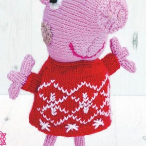 Peut inclure: Poupée cochon tricotée à la main, rose, vêtue d'un pull rouge à motifs flocons de neige blancs. Le cochon a des yeux noirs, une bouche rose cousue et des chaussures noires. Un jouet charmant et fantaisiste.