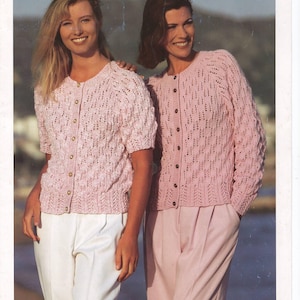 May include: A vintage knitting pattern cover showing two women in matching pink cardigans. The cardigans have a button-up design and a textured knit pattern. The text "SIRDAR Double Knitting" is at the top, and the brand name "SIRDAR" is at the bottom.