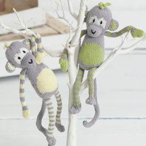 Könnte beinhalten: Zwei gestrickte Affen in Grau und Grün, die an einem weißen Ast hängen. Die Affen haben gelbe und grüne Details an Bauch, Armen und Beinen. Einer hängt, der andere sitzt.