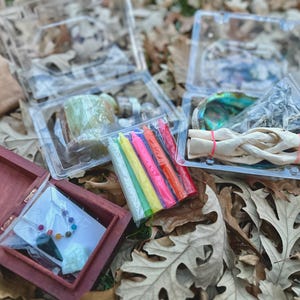 May include: A wooden box with a necklace and a crystal inside. There are also several small plastic containers with colorful candles, a seashell, and a white stick of incense.