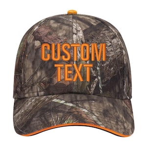 May include: A camouflage baseball cap with an orange brim and the text "CUSTOM TEXT" embroidered in orange on the front.
