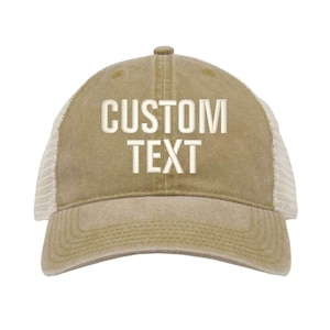 Może przedstawiać: Czapka trucker w kolorze khaki z siateczką z tyłu w kolorze białym. Na przodzie czapki wyszyty jest biały napis "CUSTOM TEXT".
