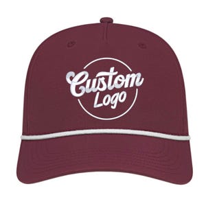 Könnte beinhalten: Burgunderfarbene Baseballkappe mit weißem Seildetail und gebogenem Schirm. Auf der Kappe steht in weißer, kursiver Schrift "Custom Logo" in einem weißen Kreis. Die Kappe hat eine strukturierte Passform und einen Knopf oben.