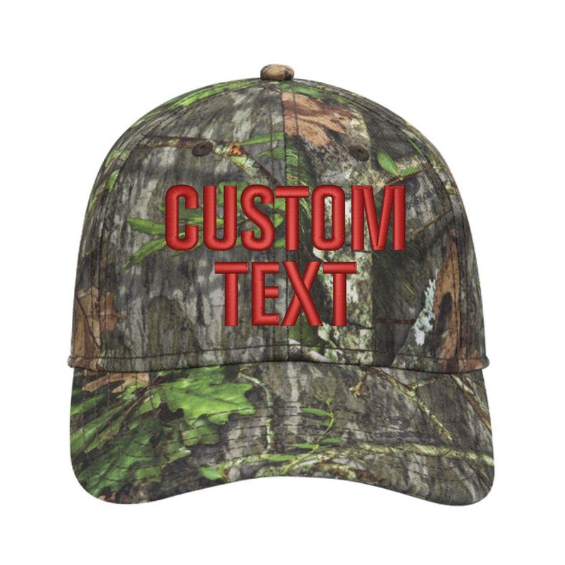 May include: A camouflage baseball cap with the words "CUSTOM TEXT" embroidered in red. The cap features a curved brim and a button on top. The pattern includes shades of green, brown, and tan.
