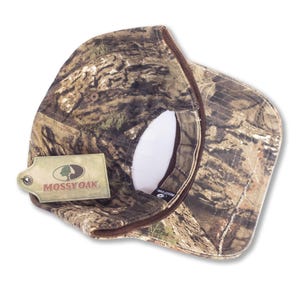 May include: A camouflage baseball cap with a brown brim and a white interior. The cap features the Mossy Oak logo on a tag attached to the side. The cap is designed with a woodland pattern.