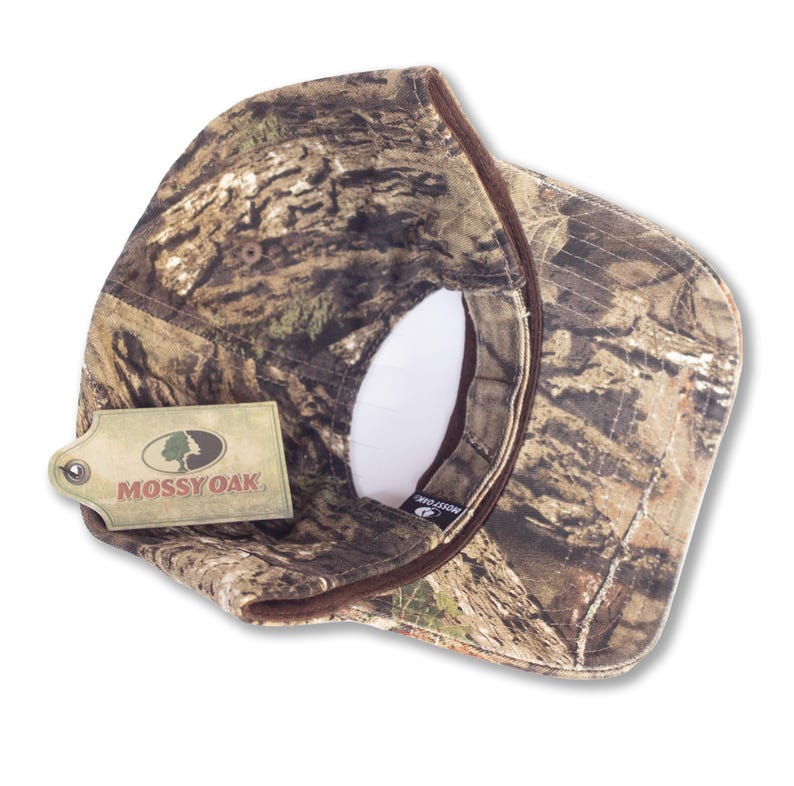 May include: A camouflage baseball cap with a brown brim and a white interior. The cap features the Mossy Oak logo on a tag attached to the side. The cap is designed with a woodland pattern.
